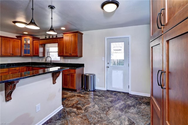 kitchen with brown cabinets, pendant lighting, a sink, a kitchen breakfast bar, and glass insert cabinets