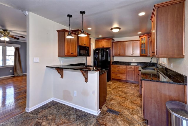 kitchen featuring brown cabinetry, a breakfast bar, a peninsula, a sink, and black appliances