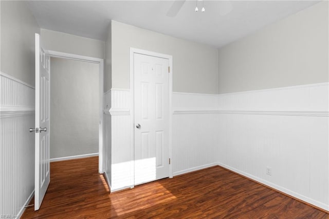 unfurnished bedroom with ceiling fan, a wainscoted wall, and wood finished floors