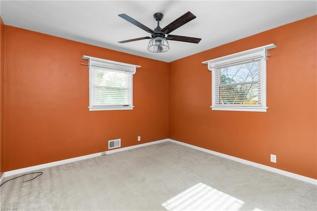 carpeted empty room with visible vents, plenty of natural light, baseboards, and a ceiling fan