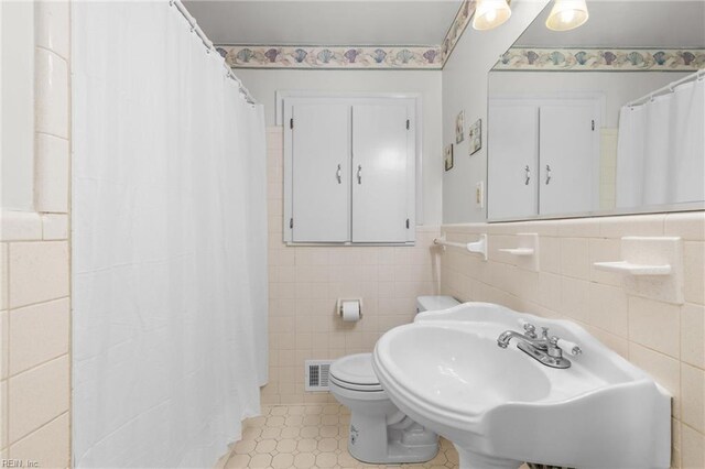 full bath featuring visible vents, a wainscoted wall, toilet, tile walls, and a sink