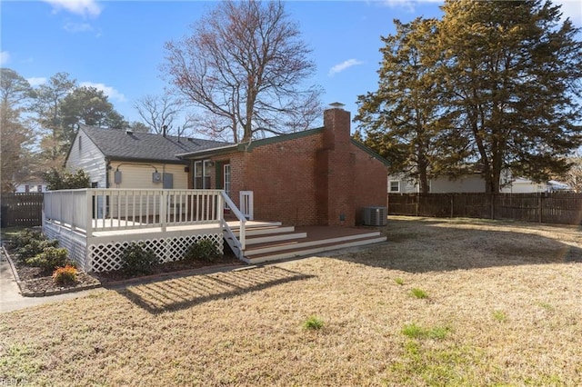 rear view of property featuring fence, a yard, a wooden deck, brick siding, and a chimney