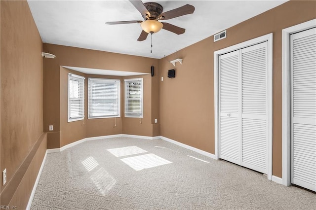 unfurnished bedroom featuring visible vents, multiple closets, a ceiling fan, carpet floors, and baseboards