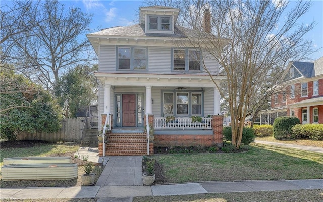 american foursquare style home featuring covered porch, a front yard, and fence