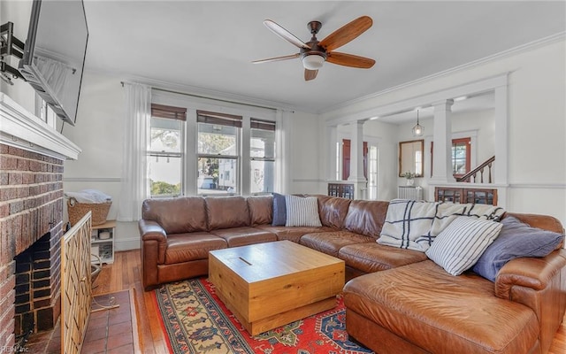 living room featuring ornamental molding, ornate columns, a fireplace, hardwood / wood-style flooring, and a ceiling fan