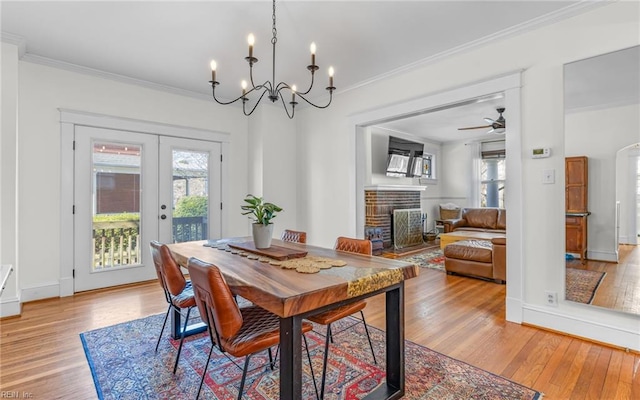 dining space with french doors, a fireplace, crown molding, and light wood finished floors