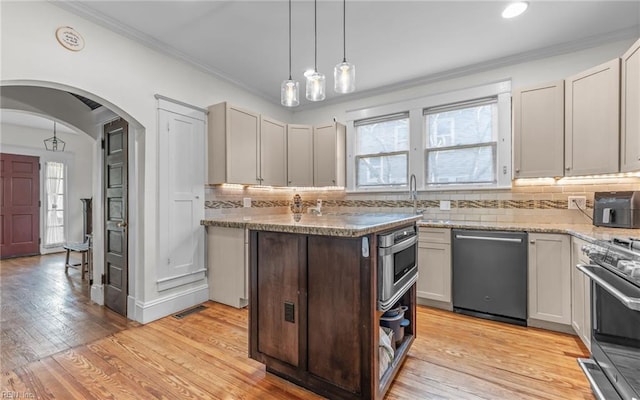 kitchen with light wood finished floors, a sink, ornamental molding, appliances with stainless steel finishes, and a wealth of natural light