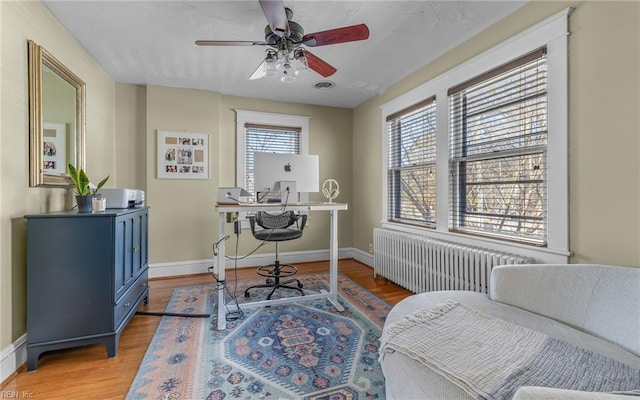 office featuring visible vents, baseboards, light wood-type flooring, radiator heating unit, and a ceiling fan