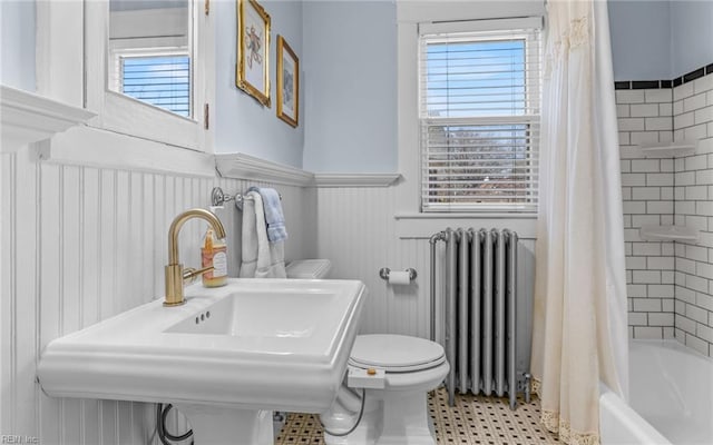 bathroom featuring radiator heating unit, a sink, wainscoting, toilet, and shower / tub combo with curtain