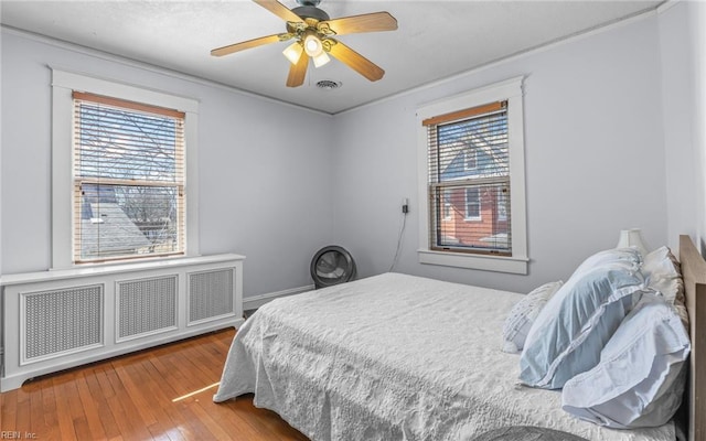 bedroom featuring visible vents, wood-type flooring, multiple windows, and a ceiling fan