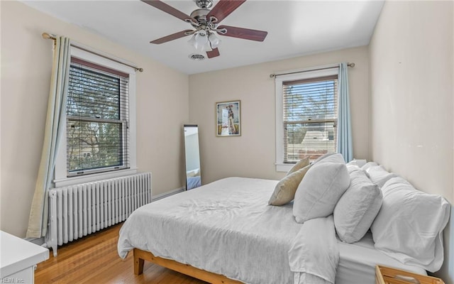 bedroom featuring radiator, visible vents, light wood finished floors, and ceiling fan