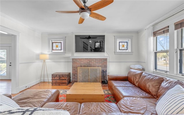 living area with ceiling fan, wood finished floors, a brick fireplace, and ornamental molding