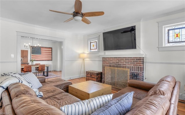 living room featuring a healthy amount of sunlight, a fireplace, crown molding, and ceiling fan with notable chandelier