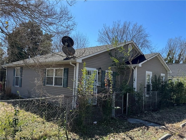 view of side of property featuring a fenced front yard and a shingled roof