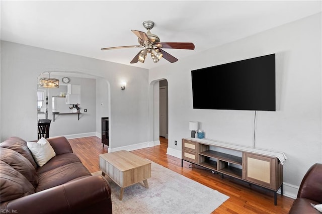 living room with arched walkways, baseboards, a ceiling fan, and wood finished floors