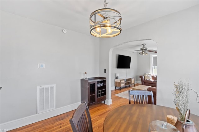 dining room with visible vents, ceiling fan with notable chandelier, wood finished floors, arched walkways, and baseboards