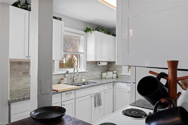 kitchen featuring light stone counters, backsplash, white cabinets, and a sink