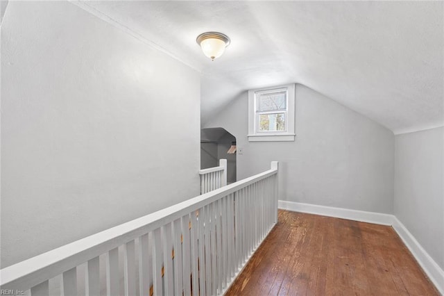 corridor with an upstairs landing, vaulted ceiling, baseboards, and wood-type flooring