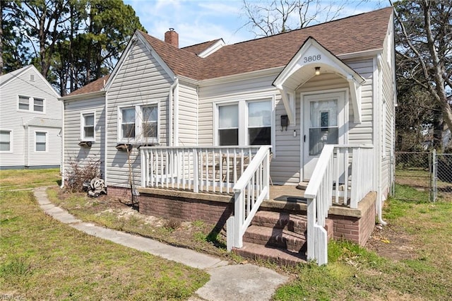 view of front of house featuring a front yard, fence, roof with shingles, and a chimney