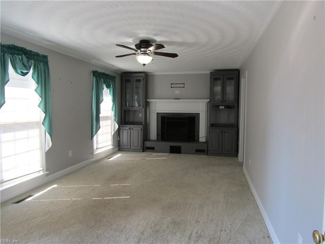 unfurnished living room featuring visible vents, a fireplace with raised hearth, baseboards, carpet floors, and a ceiling fan