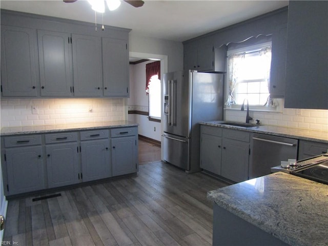 kitchen with light stone countertops, dark wood-style flooring, a sink, decorative backsplash, and appliances with stainless steel finishes