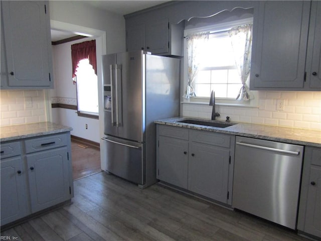 kitchen with light stone countertops, wood finished floors, a sink, stainless steel appliances, and backsplash