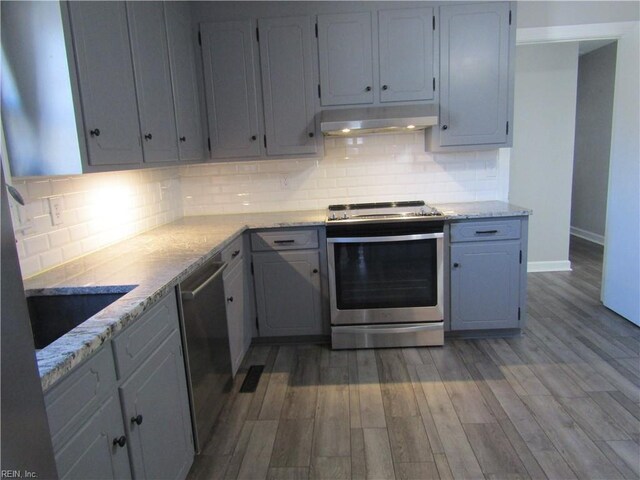 kitchen with under cabinet range hood, appliances with stainless steel finishes, tasteful backsplash, and light wood-style floors