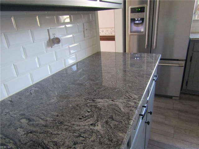 kitchen featuring dark stone countertops, decorative backsplash, a peninsula, and stainless steel refrigerator with ice dispenser