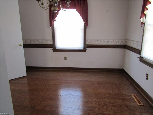 unfurnished room with visible vents, a notable chandelier, a healthy amount of sunlight, and dark wood-style flooring