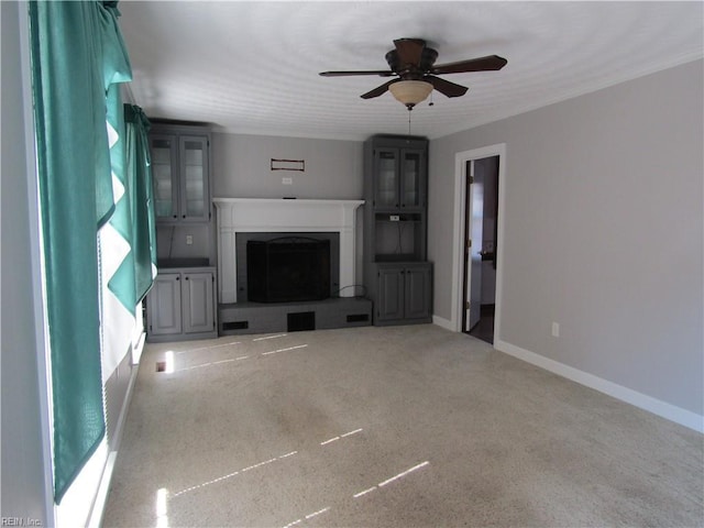 unfurnished living room featuring carpet floors, a fireplace with raised hearth, baseboards, and ceiling fan