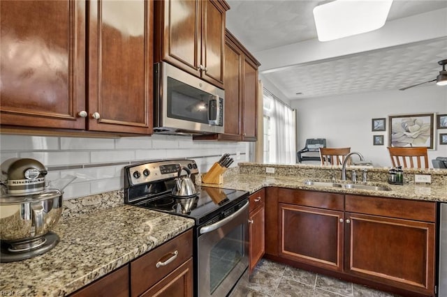 kitchen featuring tasteful backsplash, light stone counters, a peninsula, stainless steel appliances, and a sink