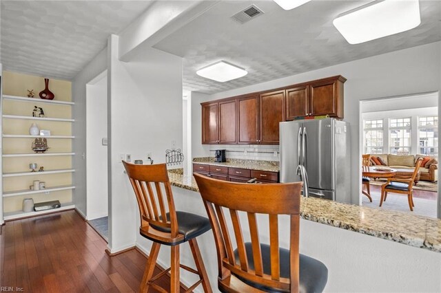 kitchen featuring visible vents, freestanding refrigerator, dark wood-type flooring, and light stone countertops