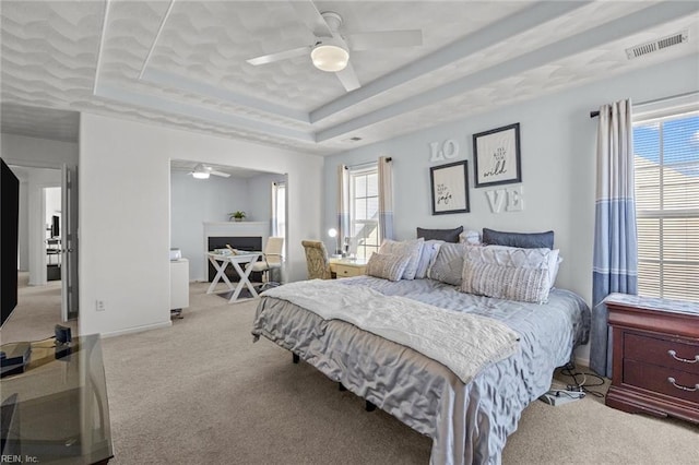 carpeted bedroom with visible vents, a raised ceiling, and ceiling fan