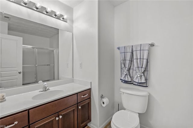 bathroom with vanity, baseboards, visible vents, toilet, and a shower with door