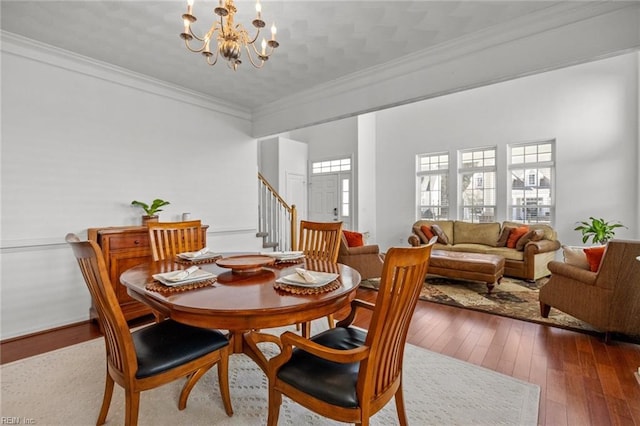 dining area featuring stairs, wood-type flooring, an inviting chandelier, and crown molding