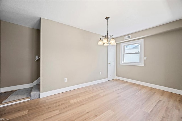 spare room featuring visible vents, baseboards, an inviting chandelier, and light wood finished floors