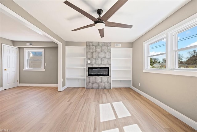 unfurnished living room featuring a tiled fireplace, visible vents, baseboards, and light wood finished floors