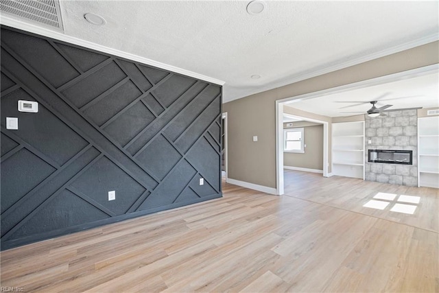 unfurnished living room featuring built in features, visible vents, light wood-style flooring, crown molding, and a large fireplace