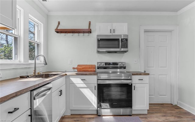 kitchen featuring ornamental molding, appliances with stainless steel finishes, wood finished floors, white cabinets, and a sink