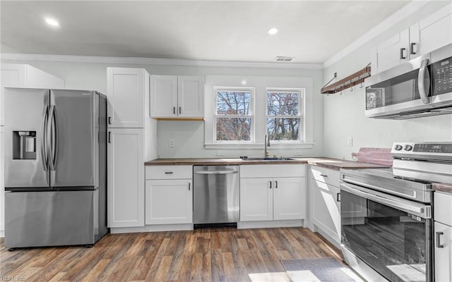 kitchen featuring dark wood-style flooring, a sink, ornamental molding, stainless steel appliances, and white cabinets