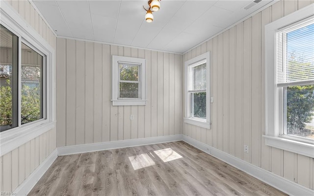 empty room featuring visible vents, plenty of natural light, baseboards, and wood finished floors