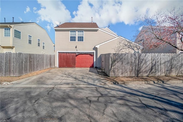 back of property with driveway, an attached garage, and fence