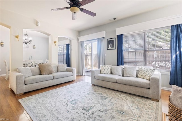 living area featuring light wood-type flooring, visible vents, ceiling fan with notable chandelier, arched walkways, and baseboards