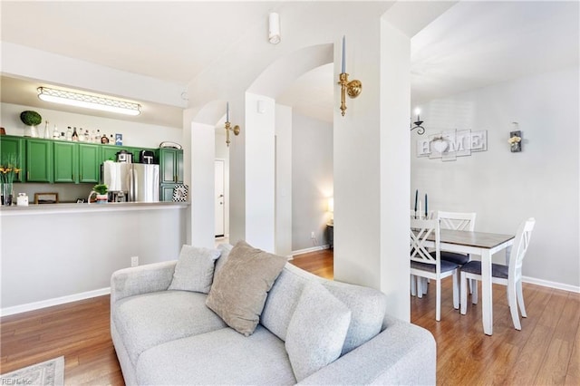 living area with light wood-style flooring, baseboards, and arched walkways