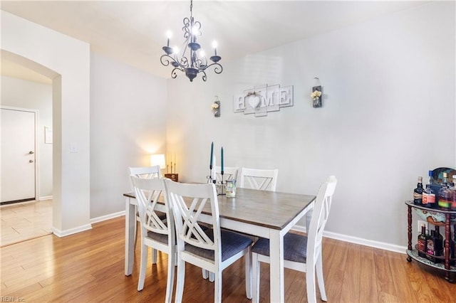 dining room with arched walkways, baseboards, light wood finished floors, and a chandelier