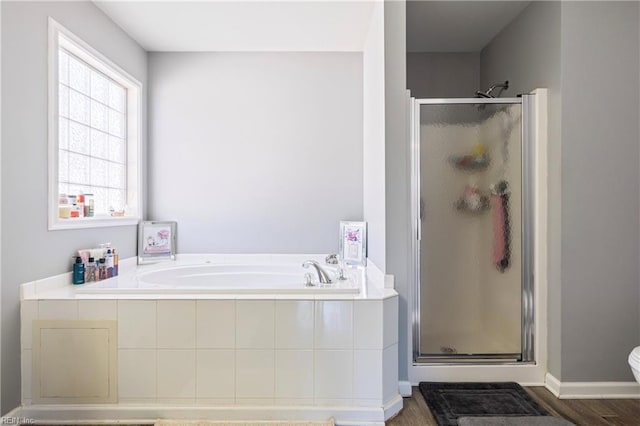 bathroom with a bath, a shower stall, baseboards, and wood finished floors