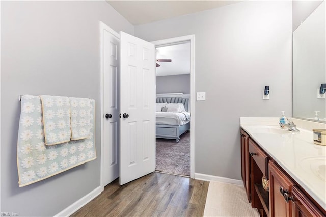 ensuite bathroom featuring connected bathroom, baseboards, double vanity, wood finished floors, and a sink