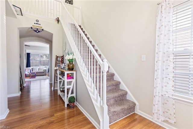 staircase featuring arched walkways, a high ceiling, baseboards, and wood finished floors