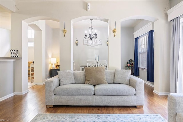 living room featuring a chandelier, arched walkways, baseboards, and wood finished floors