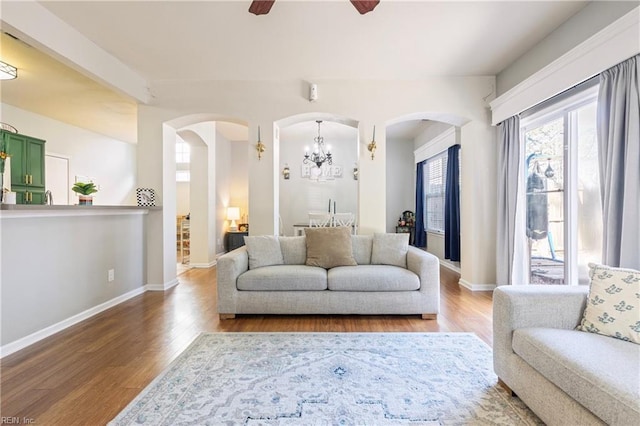 living room featuring arched walkways, baseboards, a ceiling fan, and wood finished floors